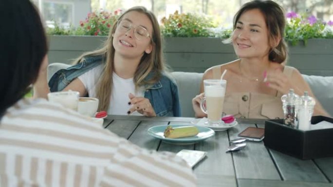 快乐的年轻女性在夏天坐在街头咖啡馆的餐桌旁享受友好的交谈。