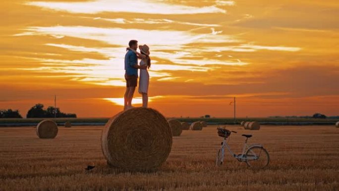 中年夫妇站在田间的干草捆上拥抱和亲吻的手持慢动作镜头