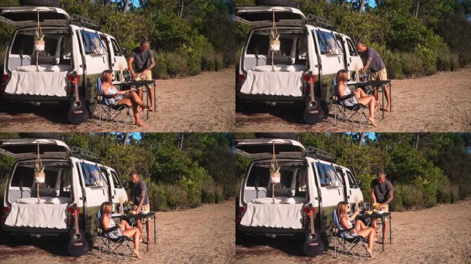 一对夫妇享受水果小吃，坐在海滩上一辆未包装的露营货车旁边