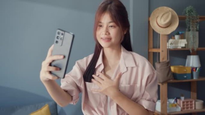 快乐无忧无虑的年轻亚洲女孩使用智能手机视频通话享受与大学朋友在家里的客厅聊天。社会距离冠状病毒大流行