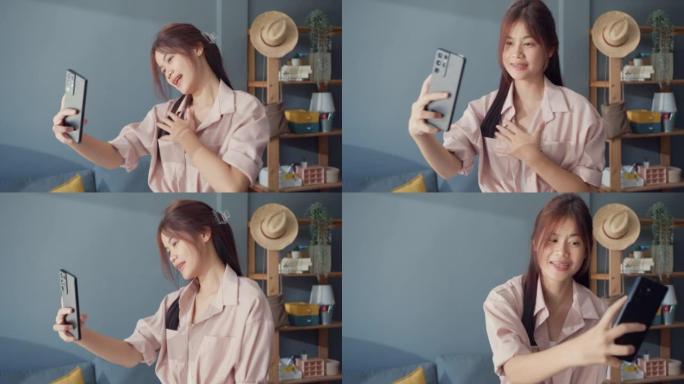 快乐无忧无虑的年轻亚洲女孩使用智能手机视频通话享受与大学朋友在家里的客厅聊天。社会距离冠状病毒大流行