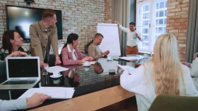 快乐的印度男老板，团队领导发言，在现代办公桌会上组同事之前使用挂图。