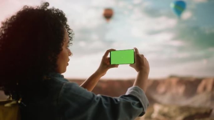 激动的年轻多民族旅行者，拥有非洲发型，在手机上拍摄智能手机照片，绿屏显示落基峡谷谷。山区国家公园的热