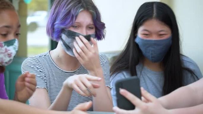 四个戴口罩的女孩嘲笑智能手机