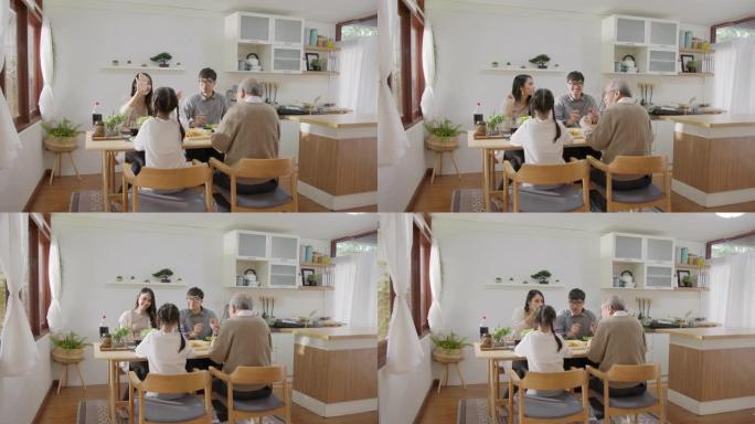 宽镜头: 快乐的亚洲家庭一起享用早餐。开朗的父母，祖父和可爱的女儿一起在家里的餐桌上享用早餐。精彩时