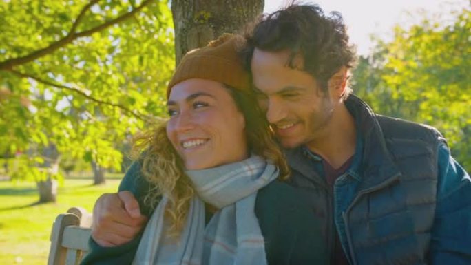 幸福的情侣微笑着坐在秋季公园的长凳上拥抱