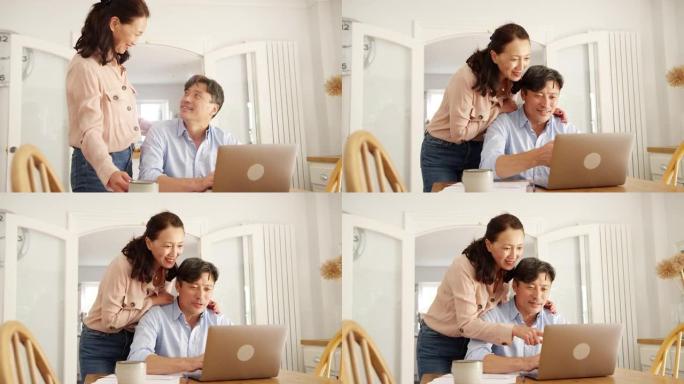 成熟的亚洲女性在家里给丈夫带来咖啡，他们一起用笔记本电脑检查家庭账单 -- 慢动作拍摄