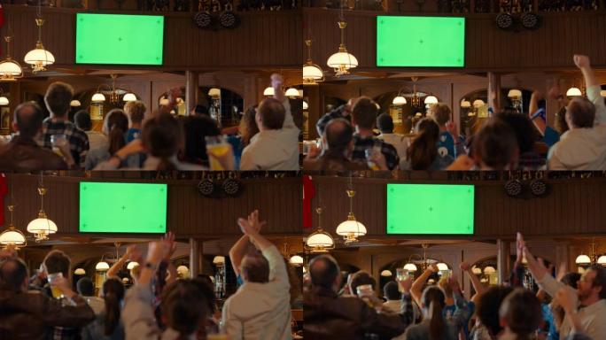 一群朋友在酒吧里通过绿屏模拟显示在电视上观看现场体育比赛。激动的球迷欢呼雀跃。年轻人庆祝球队进球并获