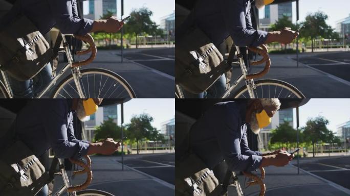 非裔美国高级男子戴着口罩，一边用智能手机靠在自行车上