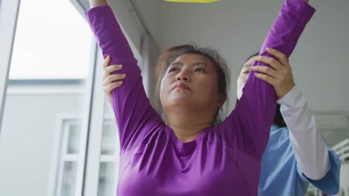 亚洲女性理疗师在手术中帮助女性患者用运动带锻炼手臂