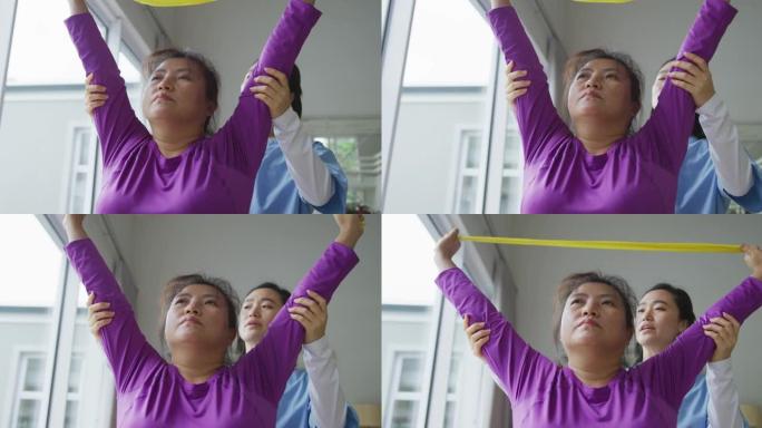 亚洲女性理疗师在手术中帮助女性患者用运动带锻炼手臂