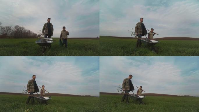 爸爸和儿子带着独轮车穿过田野。慢动作