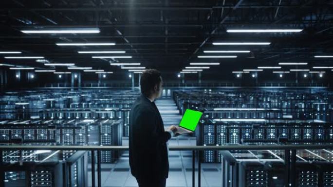 在数据中心使用色度键笔记本电脑的IT专家肖像。大服务器场云计算设施，男性维护管理员使用绿屏计算机。中