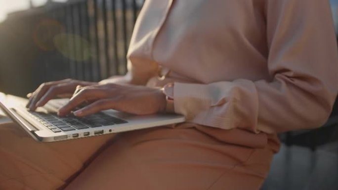 一位年轻女商人在傍晚的阳光下在笔记本电脑上打字的手