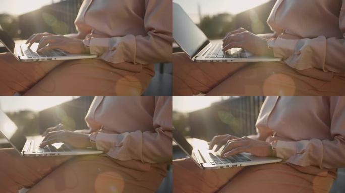 一个皮肤黝黑的女人的手在一个好的手腕上看着她的笔记本电脑在傍晚的阳光下打字，