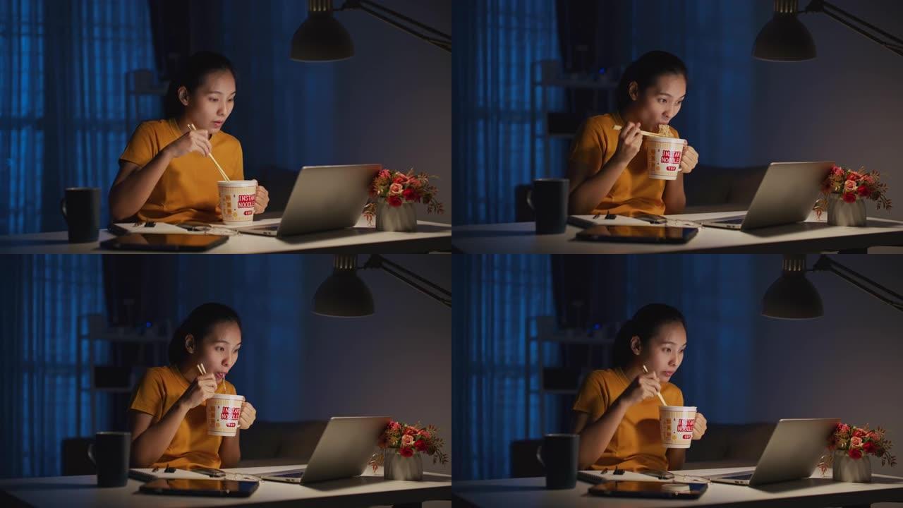 亚洲年轻女子晚上在办公室工作时吃面