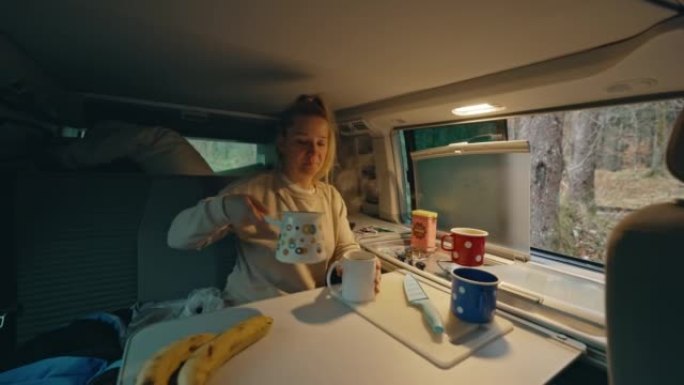 金发碧眼的女人早上坐在面包车里，把壶里的咖啡放在杯子里，把杯子给她的丈夫