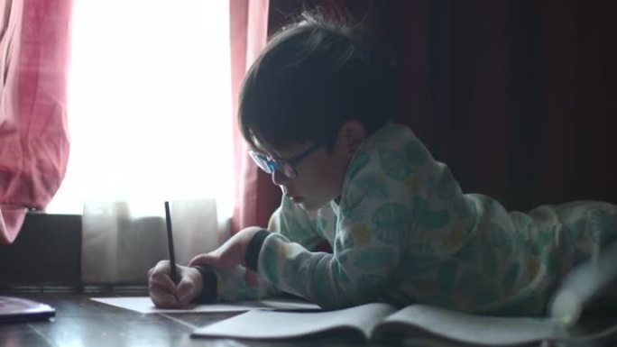 一个亚洲男孩正躺在家里专心做作业。由于Covid 19，人们无法外出生活，这是一种新的学习方式。