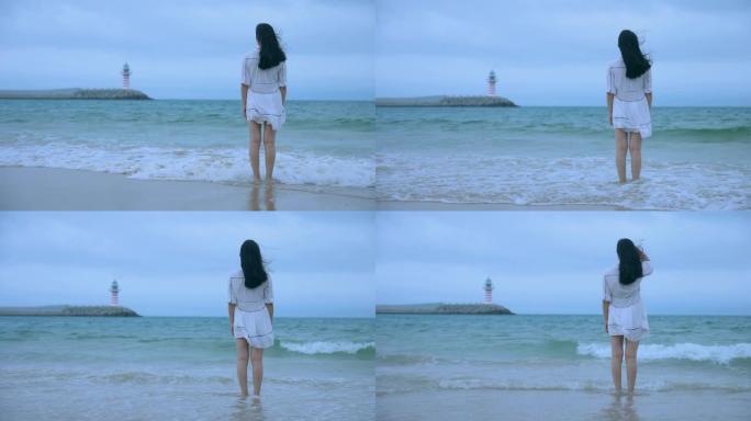 看着站在海滩上的灯塔的年轻女性