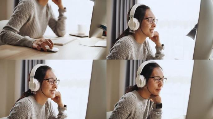 亚洲妇女在家里使用电脑时戴着耳机听音乐