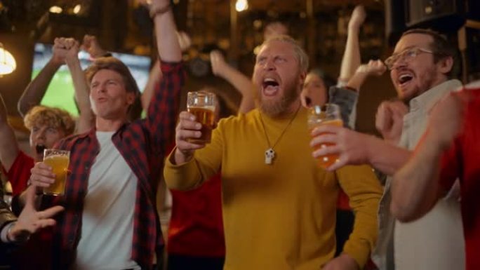 足球俱乐部成员为他们的球队欢呼，在酒吧里喝啤酒。支持球迷站在酒吧里，欢呼，举杯并大喊大叫。朋友在进球