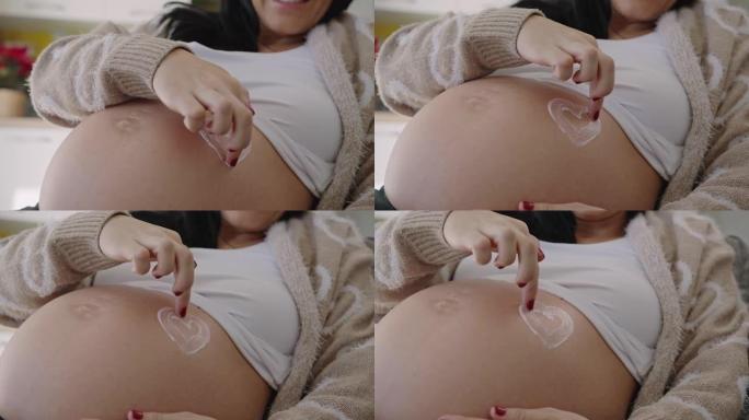 怀孕后期的SLO MO年轻女子用手指在肚子上画一颗心