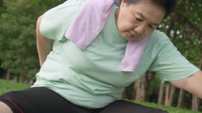 POV手持特写镜头: 亚洲高级女性在公园跑步后伸展手臂和身体进行锻炼。老运动女人扭动身体，早上感到放
