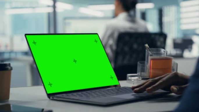 成功的黑人商人坐在办公桌前，在办公室里用绿屏笔记本电脑工作。非裔美国商人在色度键计算机上使用触摸板。