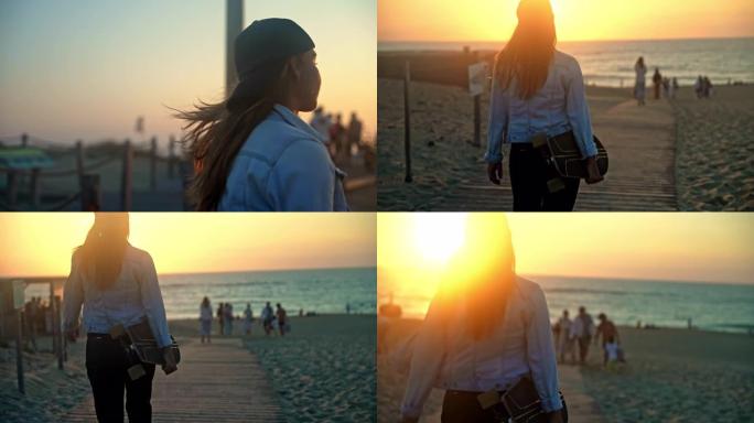 日落时，棕色头发的女人看着风景，一边走到海滩，一边在手臂下拿着滑板