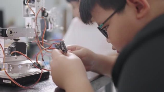 年轻的男孩和一个可爱的女孩在小学的科学课上帮助制作DIY机器人。