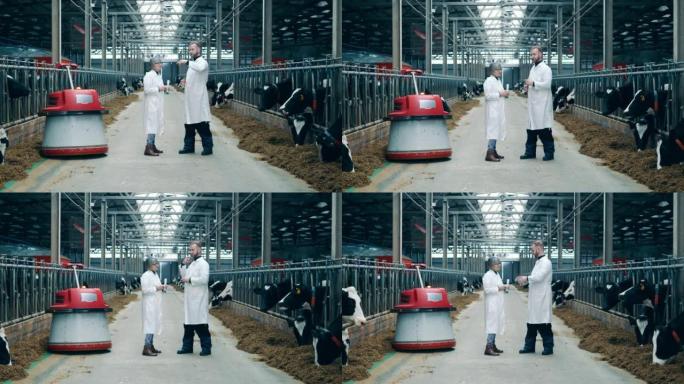 Cowshed与两名农场工人在机器人饲料推进器旁边交谈