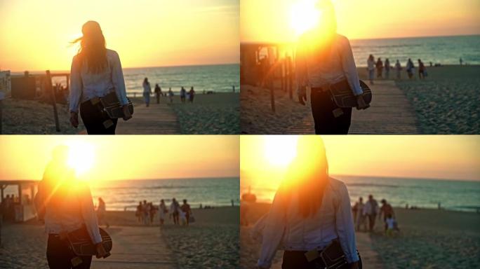 日落时，一头棕色头发的年轻女子在手臂下背着滑板走向海滩