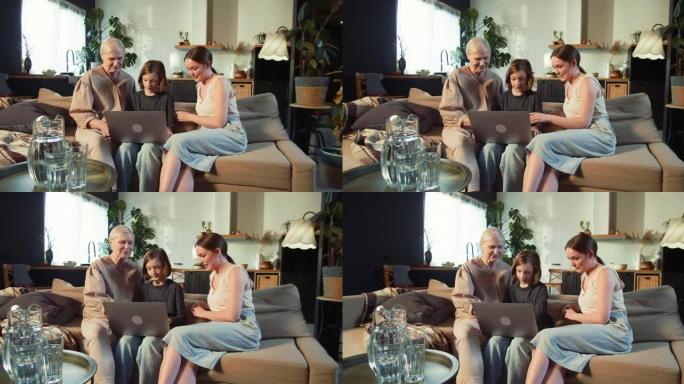 技术意识。快乐的少女与年轻的妈妈和祖母一起在家里的沙发上使用笔记本电脑。