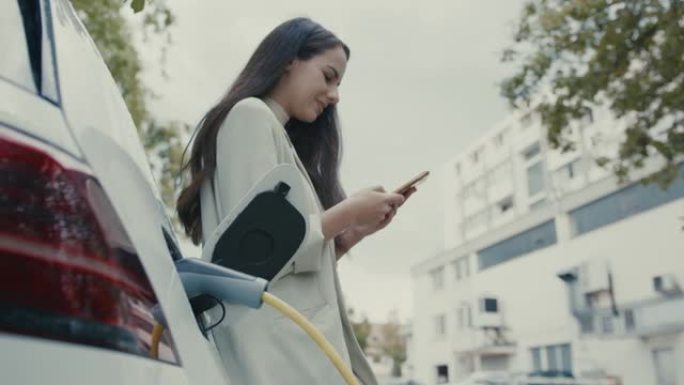 SLO MO女人在给电动汽车充电时使用手机