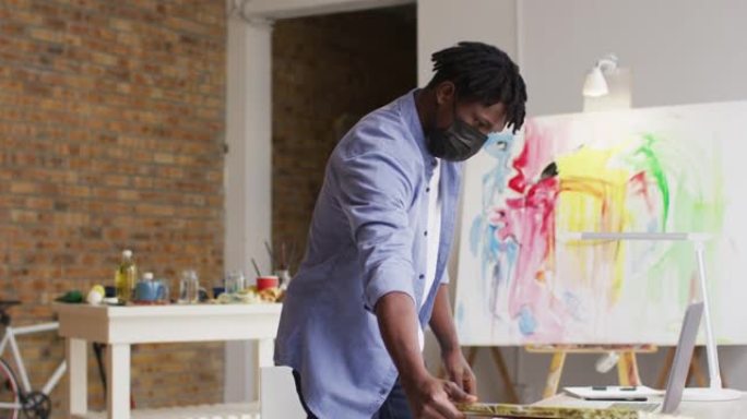 非裔美国男艺术家在art studio使用笔记本电脑戴口罩