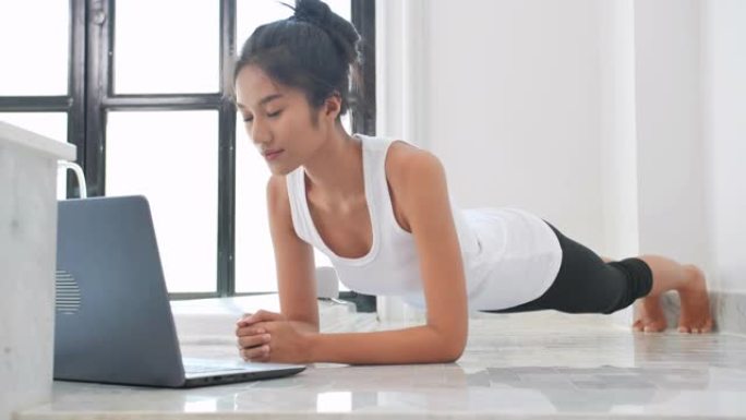 年轻的黑人妇女在笔记本电脑上做木板和观看视频，在客厅训练。家庭锻炼