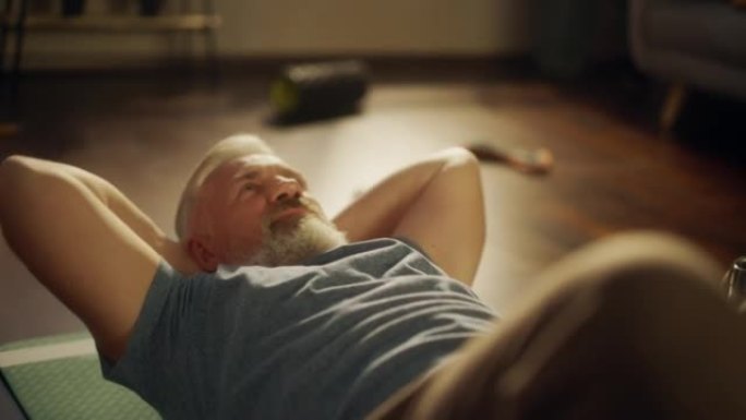 阳光明媚的早晨，一位老人在家锻炼和训练的肖像。老年男性在阁楼公寓客厅做背部和肌肉强化。健康和健身生活