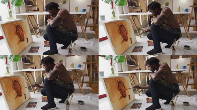 非裔美国男性艺术家在艺术工作室的画布上穿着围裙绘画的侧视图