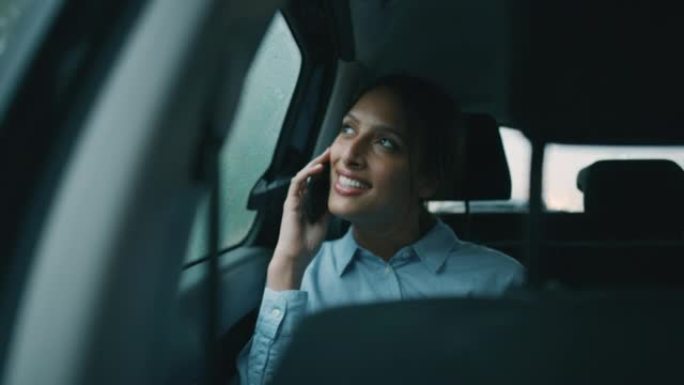 一位年轻的女商人在外面下雨时与驾驶员一起乘坐现代汽车旅行时正在用智能手机打电话。