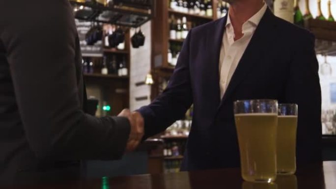 无法辨认的白人男子在酒吧享用啤酒时握手达成交易