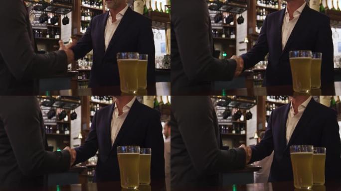 无法辨认的白人男子在酒吧享用啤酒时握手达成交易