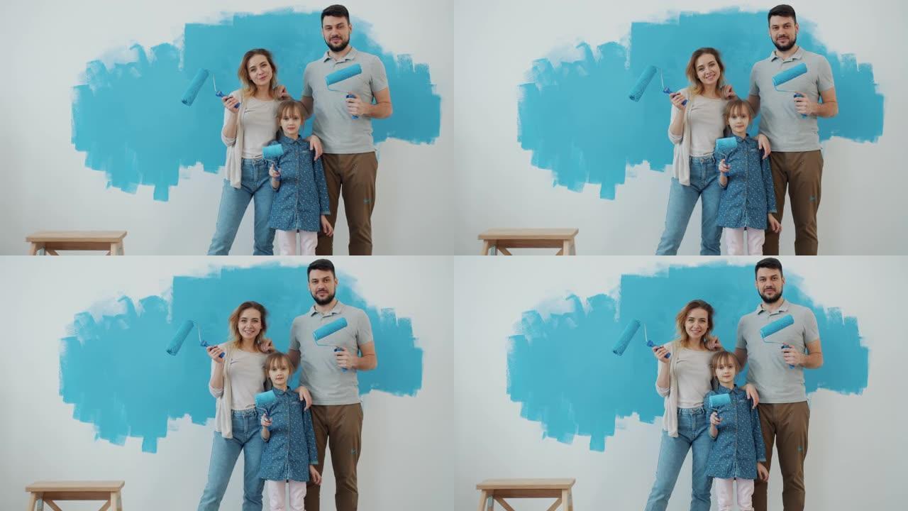 幸福家庭母亲父亲和女儿的慢动作肖像在家中室内拿着绘画滚筒