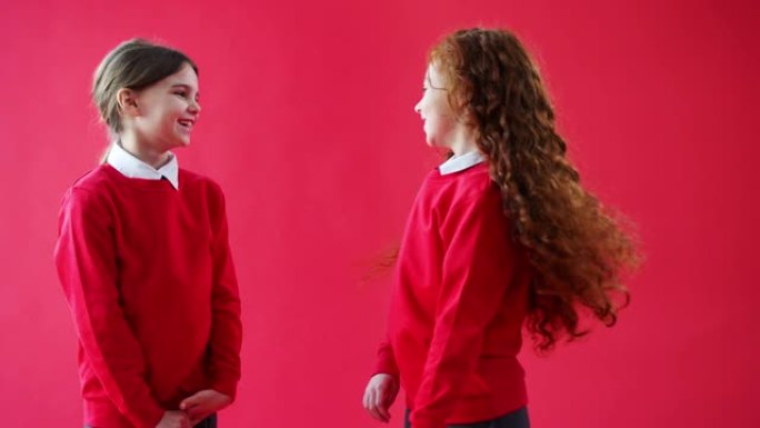 两名穿着制服的女小学生在红色工作室背景下交谈