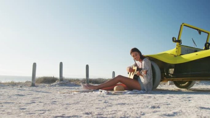 快乐的高加索女人坐在海边的沙滩车旁边弹吉他