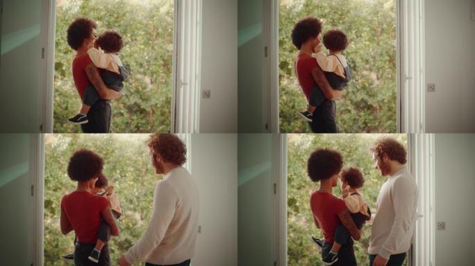 爱的混血儿家庭在现代家庭客厅拥抱和抱着可爱的男婴，看着阳台。开朗的母亲养育孩子。童年、新生活、为人父