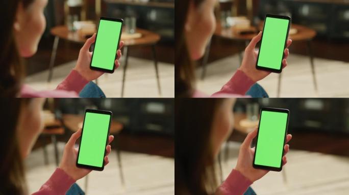 女性手握着带有绿屏模拟显示的智能手机。女性在家里休息，在移动设备上观看视频和阅读社交媒体帖子。特写镜