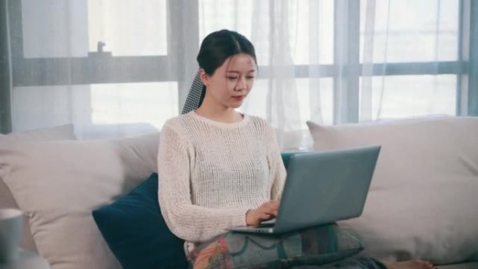 年轻女性在家中使用笔记本电脑坐在沙发上