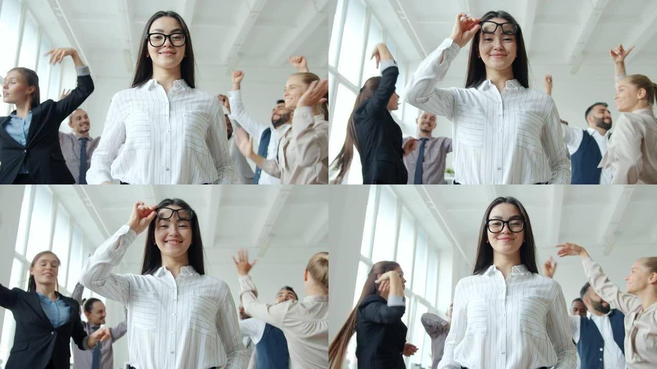美丽的亚洲女士触摸眼镜，微笑着站在公司派对上跳舞