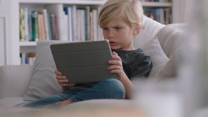 快乐小男孩使用数字平板电脑玩游戏在家沙发放松儿童在线浏览移动设备技术反社交成瘾概念4k