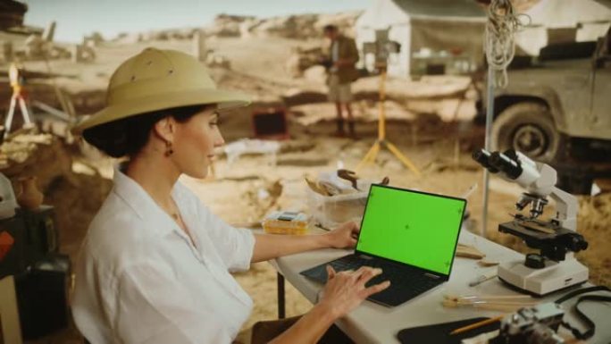 考古挖掘现场: 女性考古学家使用绿屏色键显示笔记本电脑，分析化石遗迹，古代文明文化文物。历史学家在挖